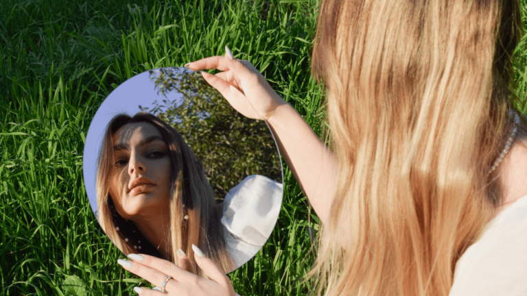 A woman gracefully holds a mirror before her in a serene field.